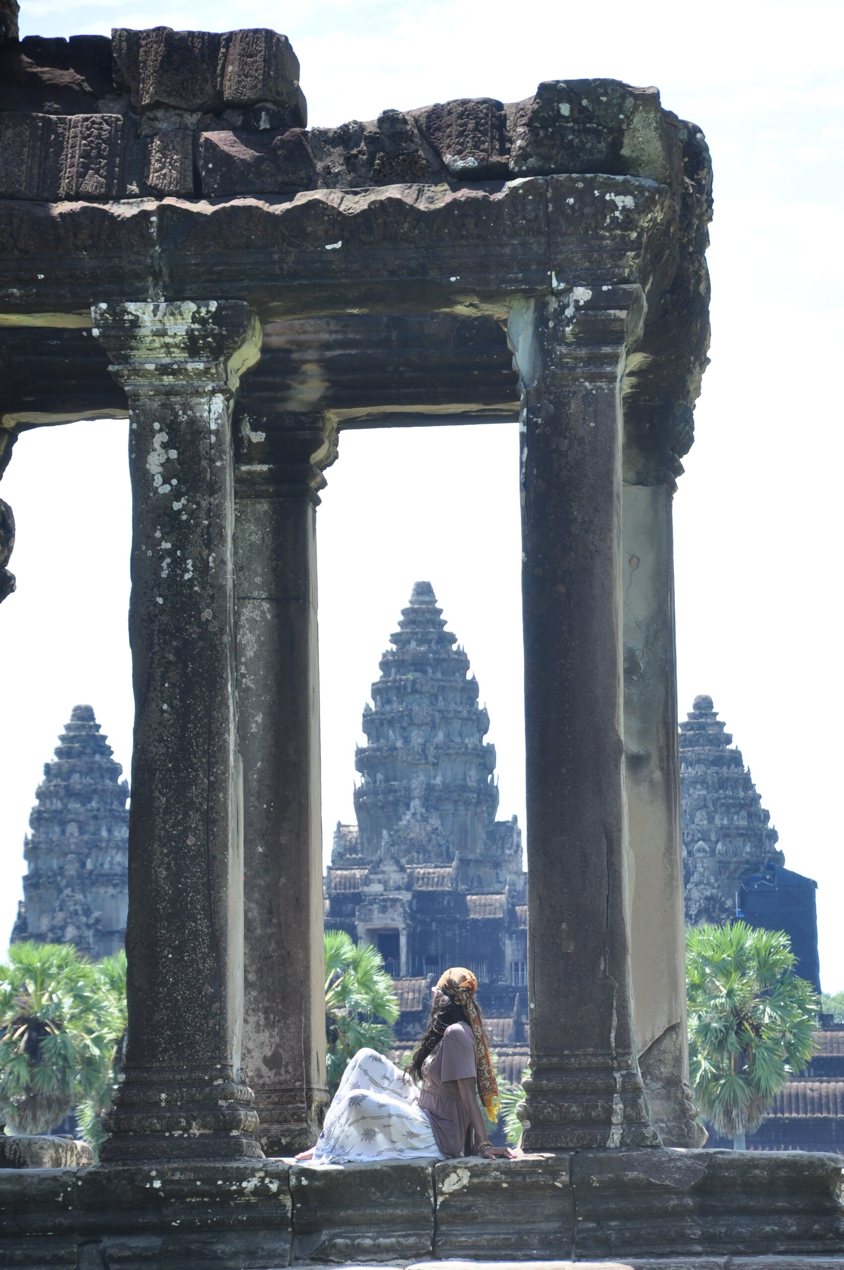 Exploring Angkor Wat: student seated between pillars overlooking the iconic Cambodian temple
