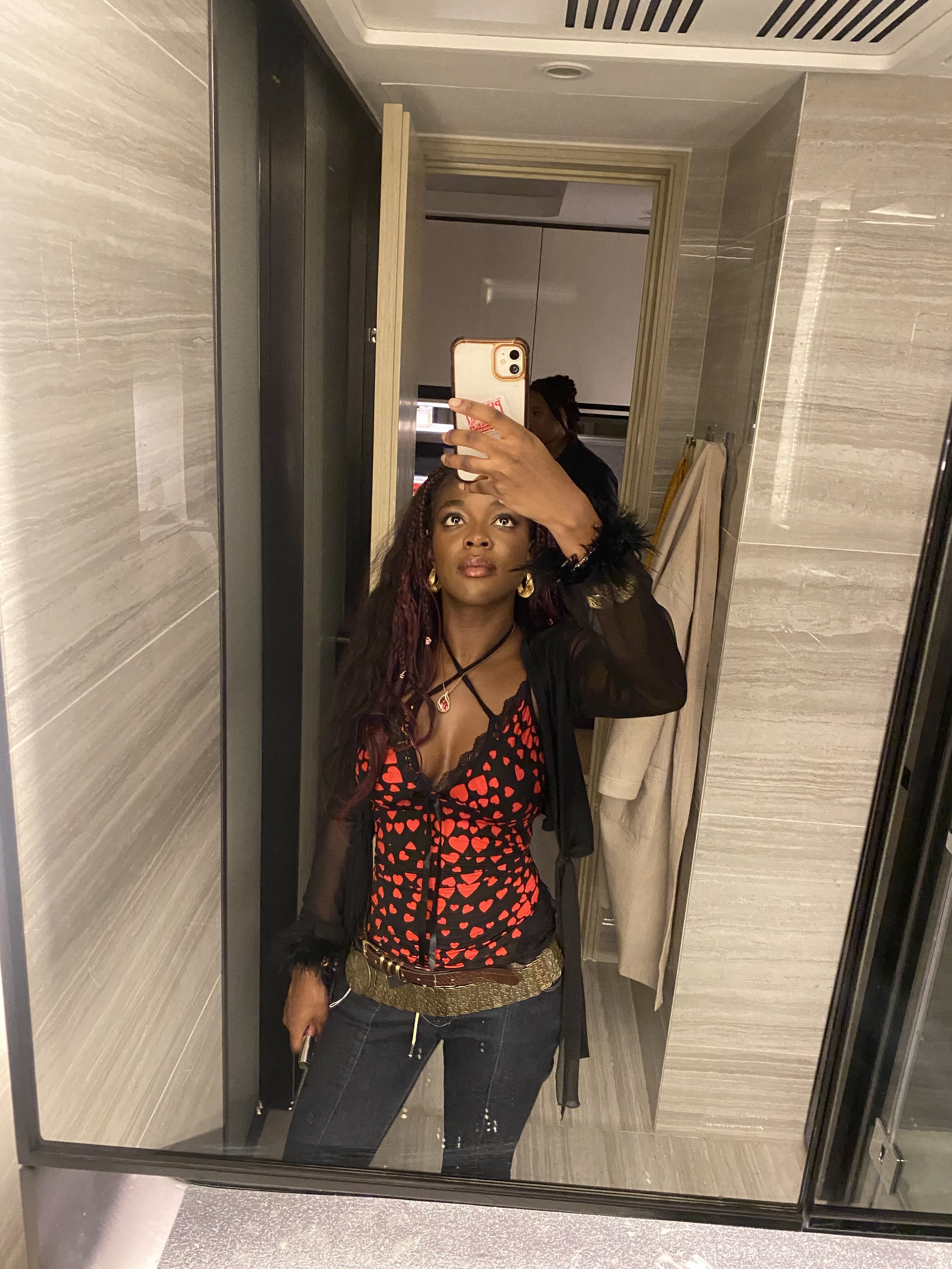 How to actually develop your personal style part 2 Y2K-inspired outfit featuring denim flares, two belts, black vest top with a red heart, and mesh black cardigan