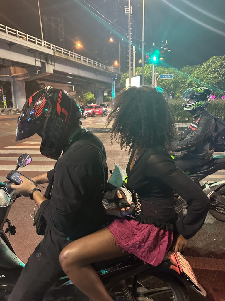 raveler riding on the back of a Grab motorbike at a traffic light in Bangkok, experiencing local transportation and daily city life in Thailand